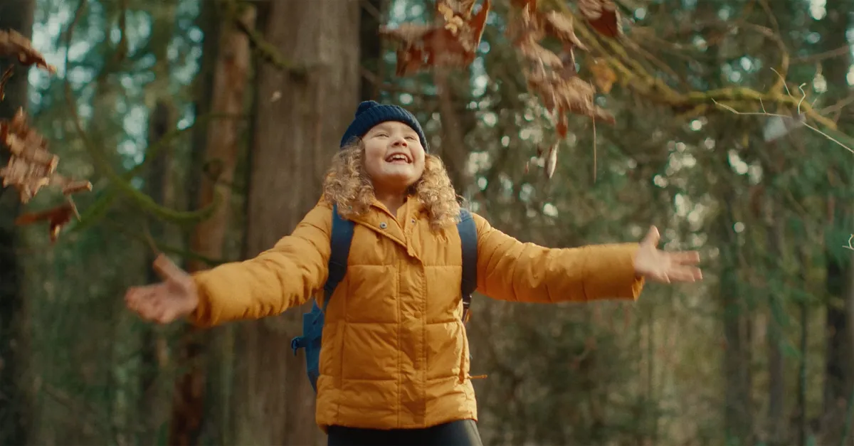 Commercials and campaign production — smiling child in yellow jacket tossing autumn leaves in a forest